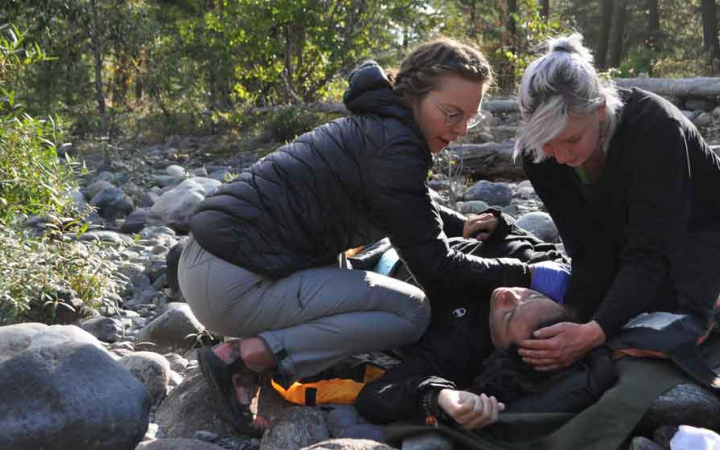 three people participate in a wilderness first responder exercise